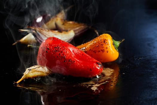 Appetizing peppers preparing with garlic and onion on black hot surface in oil