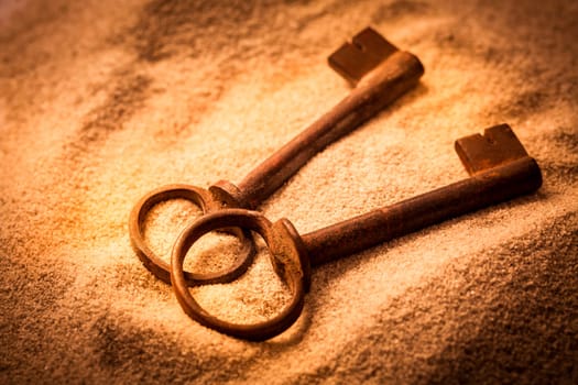 Two old rusty keys in sand in warm tones