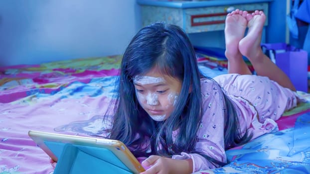 The children are playing tablet on the bed.