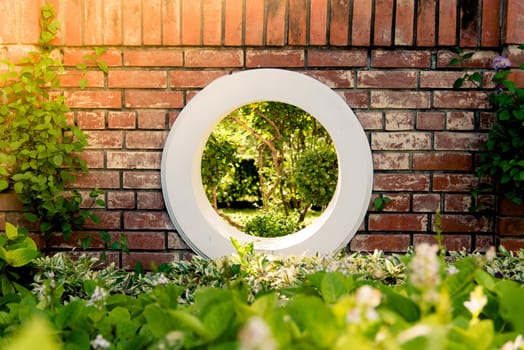 Wall brick and circle white window over green bush in the park with the sunlight.