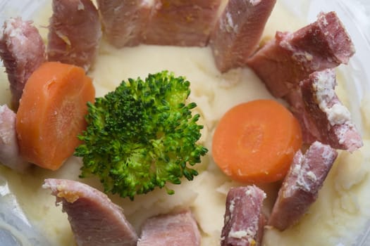 Looking down onto a plain and simple evening meal. Consisting of potato mash, gammon, broccoli and carrots. All within the plastic ready made mash tub