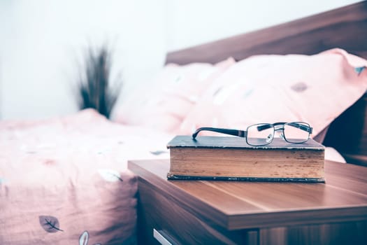 Book and eyeglasses on a nightstand table in the bedroom on a sunny morning