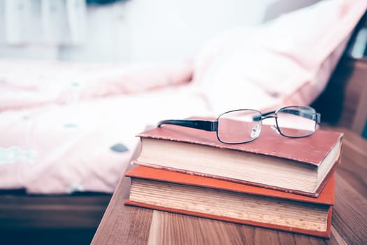 Book and eyeglasses on a nightstand table in the bedroom on a sunny morning