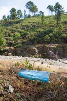 Surgical face mask threw out close to mountain river. Environmental pollution in nature concept
