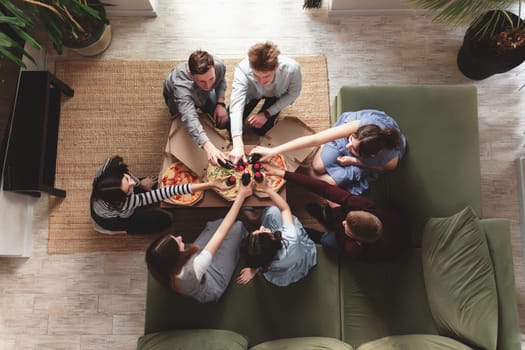 A pizza party, a group of friends chatting and happily eating pizza at the table and drinking sweet soda water. Top view from the second floor. High quality photo