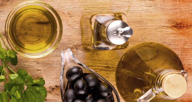 The Olive oil with fresh herbs and Black olives on wooden background