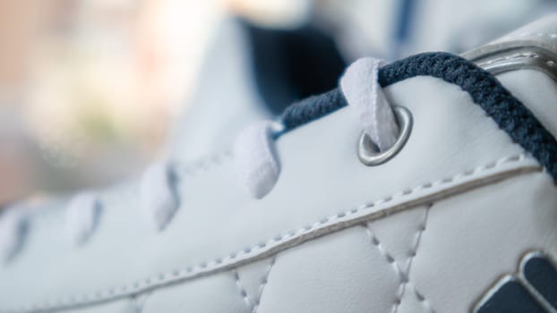 White athletic lace-up sneakers. White laces are tied close-up. Blurred background. Sports concept. Metal rivet for shoes as a detail or an element. Fashionable and stylish footwear