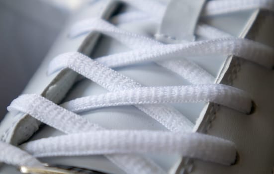 White athletic lace-up sneakers. White laces are tied close-up. Blurred background. Sports concept. Metal rivet for shoes as a detail or an element. Fashionable and stylish footwear