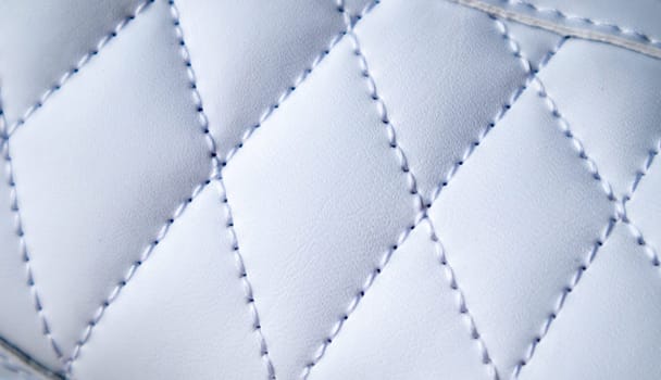 Close-up of synthetic fabric with white diamond stitching. Texture the diamond in a classic style. Luxurious background. Quilted fabric in white or light color, texture