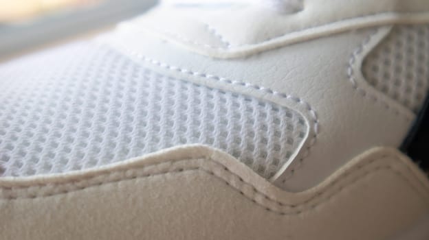 White color mesh fabric on a part of sports shoes. Running shoe net. Sportswear textured lattice. Textile texture background. Detail of a white sneaker in fabric with laces. Fragment of sports shoes