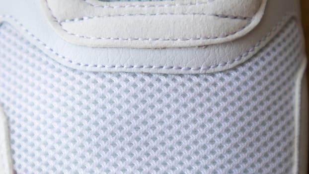White color mesh fabric on a part of sports shoes. Running shoe net. Sportswear textured lattice. Textile texture background. Detail of a white sneaker in fabric with laces. Fragment of sports shoes