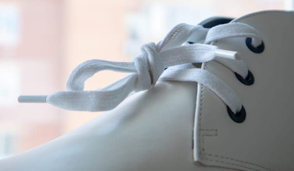 White leather sneakers lace-up shoes. White laces are tied close-up. Blurred background. Sports concept. Metal rivet for shoes as a detail or an element. Fashionable and stylish footwear