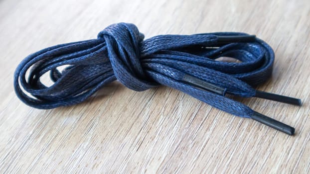 A subject shot of dark blue flat laces with thin tips for shoes rolled up and isolated on a wooden background. Stylish accessory