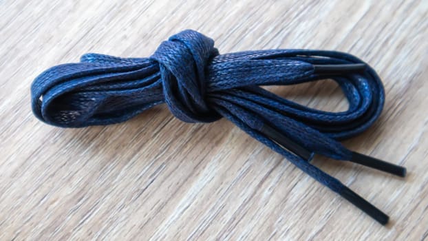 A subject shot of dark blue flat laces with thin tips for shoes rolled up and isolated on a wooden background. Stylish accessory