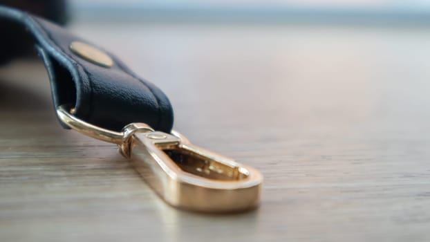Swivel carabiner fastener with leather black bag strap on a wooden background. Metal carabiner with swivel clip or hook. Small gold fittings close-up in selective focus