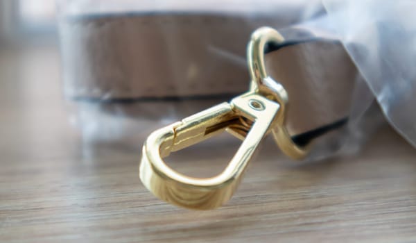Swivel snap fastener with leather beige bag strap on a wooden background. Metal carabiner with swivel clip or hook. Small gold fittings close-up in selective focus