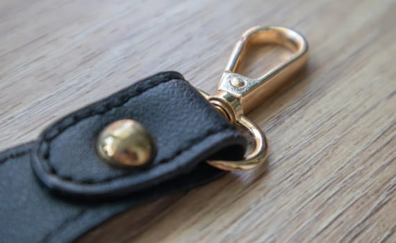 Swivel carabiner fastener with leather black bag strap on a wooden background. Metal carabiner with swivel clip or hook. Small gold fittings close-up in selective focus