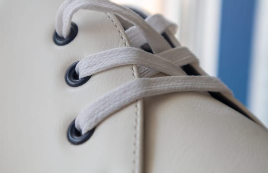 White leather sneakers lace-up shoes. White laces are tied close-up. Blurred background. Sports concept. Metal rivet for shoes as a detail or an element. Fashionable and stylish footwear