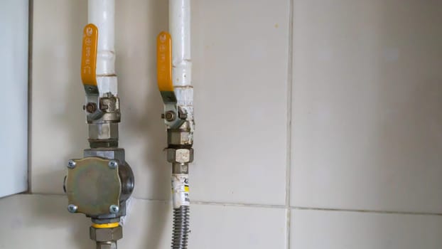 Yellow valves and natural gas pipes in a modern home boiler room in a kitchen with ceramic tiles. Gas valve ball valve, gas and plumbing equipment