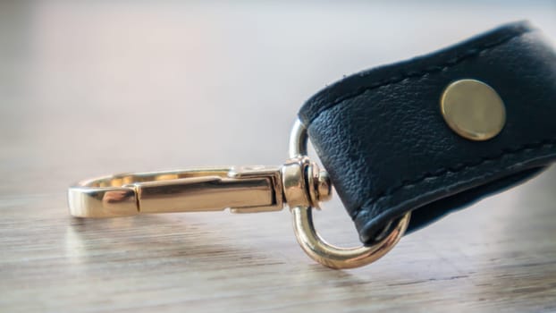 Swivel carabiner fastener with leather black bag strap on a wooden background. Metal carabiner with swivel clip or hook. Small gold fittings close-up in selective focus