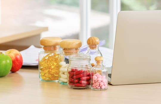 Pharmaceutical medicine and capsules with fruits and laptop computer on nutritionist doctor desk in hospital room