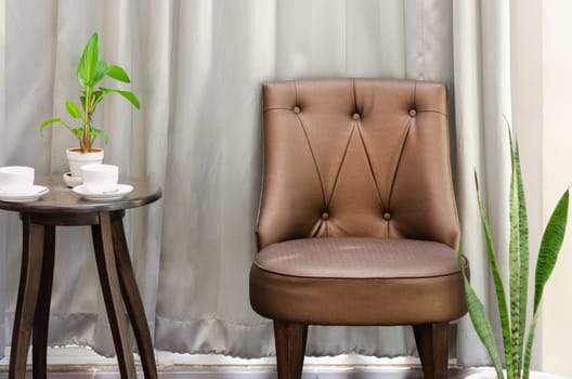 Living room or lobby interior with brown chair and round side table with coffee cup and green plant