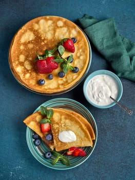 Pancakes with berries and sour cream on dark green background. Top view. Maslenitsa. Shrovetide. Shrove Tuesday. Pancake Day. Happy holiday, Greeting. Dessert. Serving food