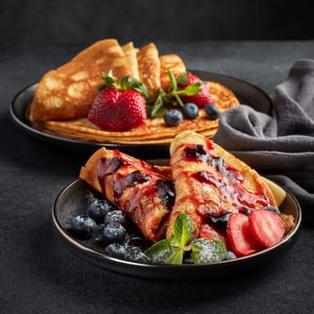 Pancakes with berries  and sweet sauce on black background.  Maslenitsa. Shrovetide. Shrove Tuesday. Pancake Day. Happy holiday, Greeting. Dessert. Serving food