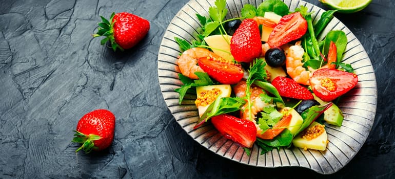 Salad with shrimps,strawberries,avocado and herbs.Seafood salad on rustic wooden background.Copy space,space for text