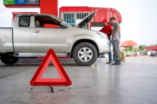Red triangle reflector roadside warning on the floor. There is a broken pickup car in the background.