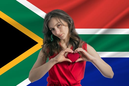 Love South African Republic. A girl holds a heart on her chest in her hands against the background of the flag of South African Republic. The concept of patriotism.