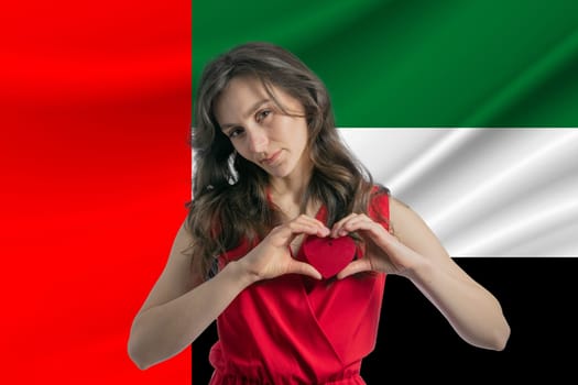 Love United Arab Emirates. A girl holds a heart on her chest in her hands against the background of the flag of United Arab Emirates. The concept of patriotism.