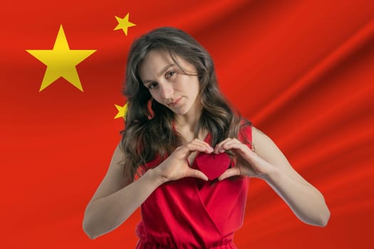 Love People's Republic of China A girl holds a heart on her chest in her hands against the background of the flag