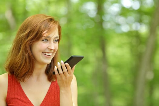 Happy woman using voice recognition on phone in a forest