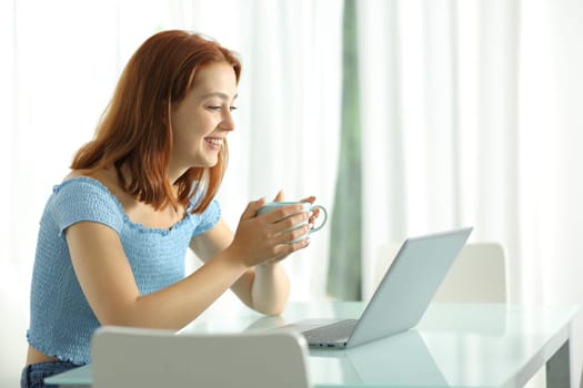 Woman watching media on laptop holding coffee cup