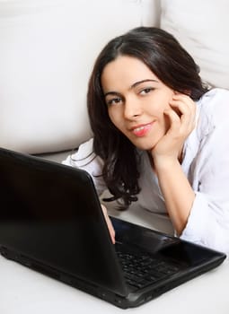 Happy young woman working on a laptop from her bedroom