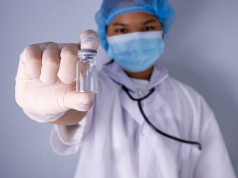 Studio portrait of a female doctor wearing a mask and wearing a hat. in the hand of the vaccine bottle and stretched out his arms in front standing on a white background. studio shot background, COVID-19 concept