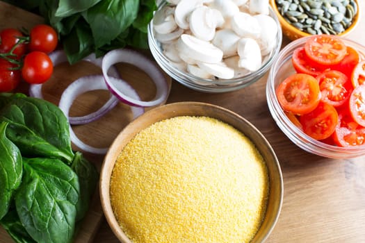 Ingredients for polenta recipe, with polenta in wooden bowl with sliced tomatoes, spinach and red onions.