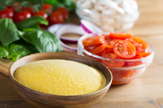 Ingredients for polenta recipe, with polenta in wooden bowl with sliced tomatoes, spinach and red onions.
