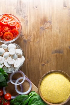 Ingredients for polenta recipe, with polenta in wooden bowl with sliced tomatoes, spinach and red onions.  Viewed from angle directly above with copy space on wooden table.  Can be used vertical or horizontal.