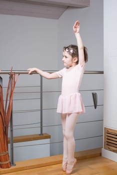 Little girl wearing a ballet dress is practicing ballet in a dance studio