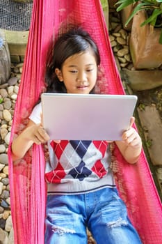 The girl lying in hammock with playing tablet pc.