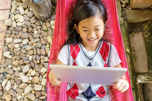 The girl lying in hammock with playing tablet pc.