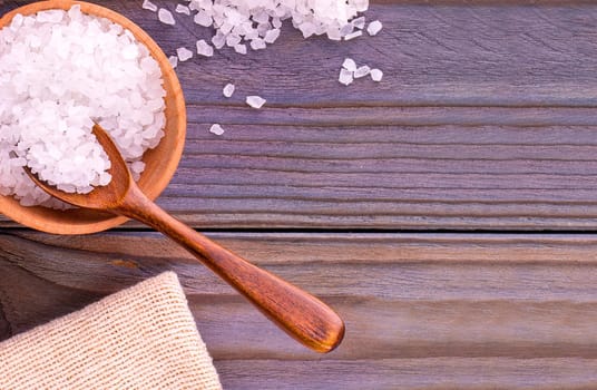 The white sea salt on cup, spoon and burlap on a wooden table