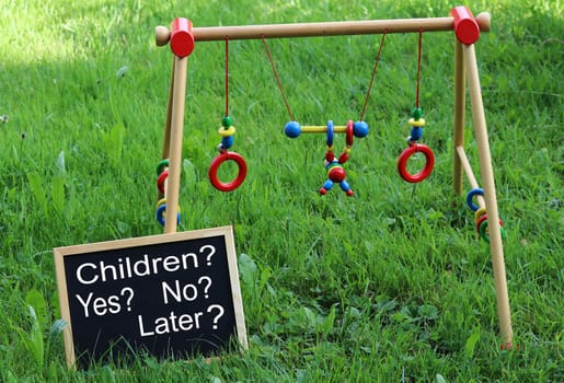 Baby toys and a blackboard in a meadow with the inscription Children? Yes? No? Later?