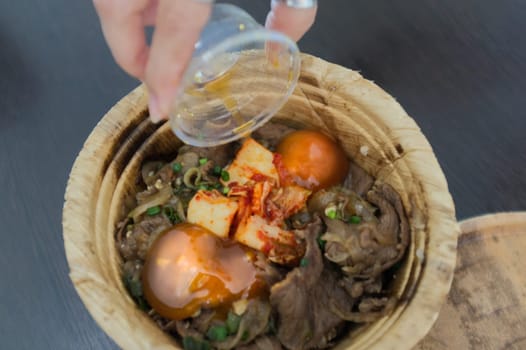 Woman hand with Japanese Gyudon with egg or Japanese beef bowl with egg in organic banan leaf bowl