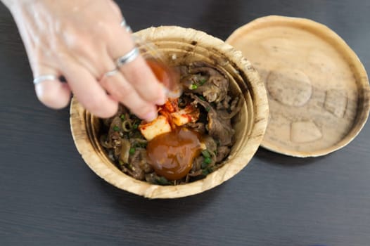 Woman hand with Japanese Gyudon with egg or Japanese beef bowl with egg in organic banan leaf bowl