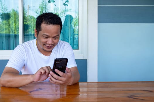 Asian man wearing white shirt using the phone on a wooden table