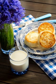 Cheesecakes or Syrniki on a plate. Russian and Belarussian cuisine, cornflowers decoration. Vertical image
