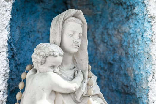 Statue of Our lady of holy rosary and child Jesus. Blue rustic concrete on background.